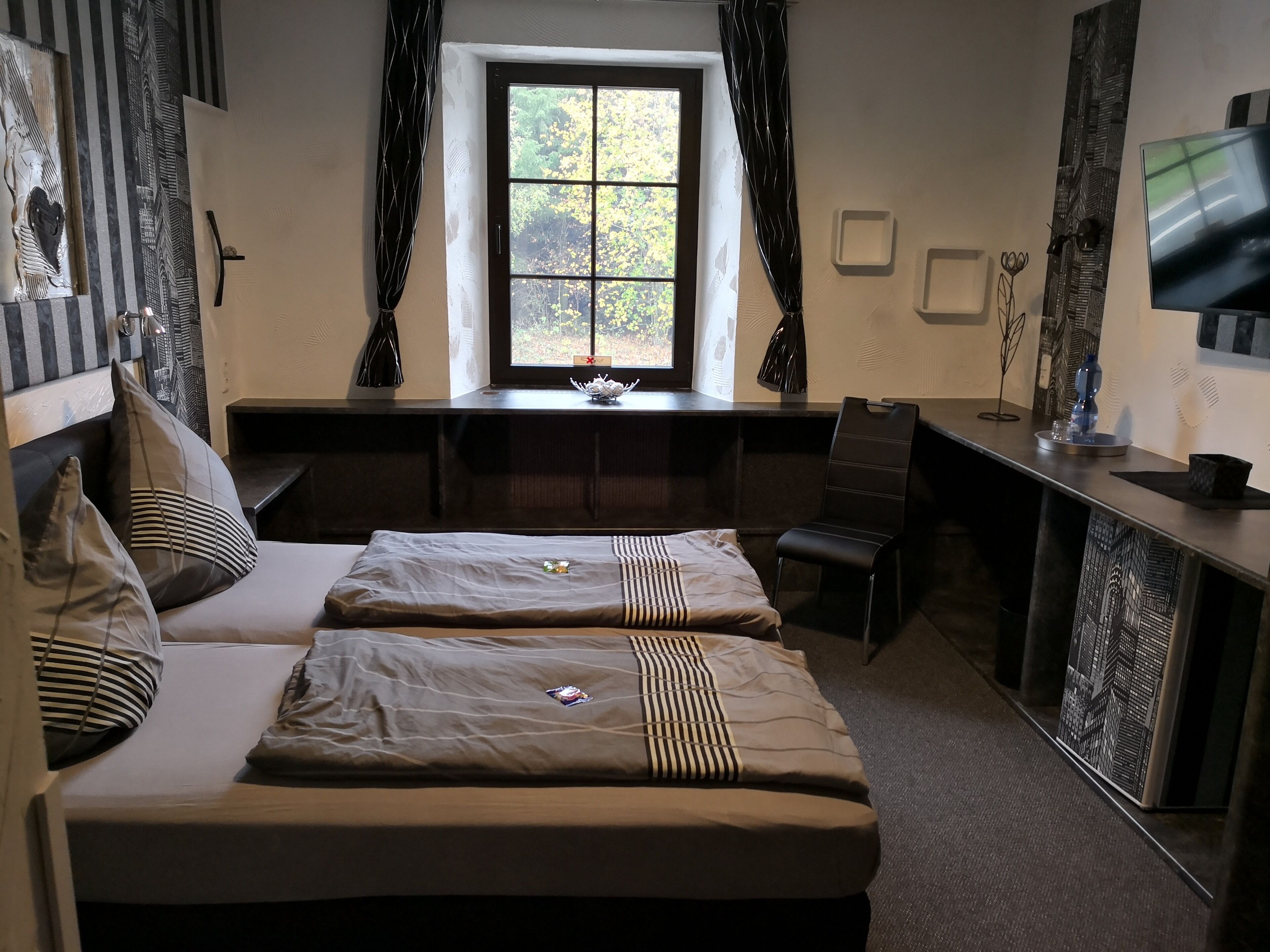 A hotel room with a large bed, a desk, a chair, a TV, and a window with curtains.