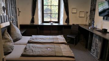 A hotel room with a large bed, a desk, a chair, a TV, and a window with curtains.