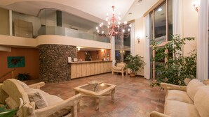 Um hall amplo com parede de destaque em pedra, um balcão de recepção e um candelabro.