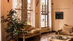 Uma sala de estar acolhedora com parede de pedra, uma janela ampla, sofá de madeira, mesa de centro e um candelabro.