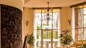 Uma escadaria imponente leva a um amplo saguão com parede de pedra decorativa, um lustre e plantas em vasos.