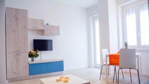 Un salon moderne doté d’un téléviseur à écran plat, d’un coin repas avec une table et des chaises, et d’un canapé.