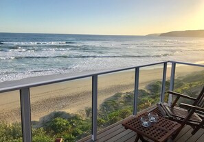 A wooden deck with a table and chairs overlooking a beach with waves. - Dune Beach House (Wilderness)