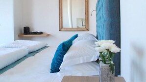 Une chambre d’hôtel avec deux lits, une étagère en bois sur laquelle se trouve un appareil photo, un miroir et un vase avec des fleurs.