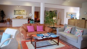 Un salon spacieux avec un canapé, des fauteuils et une table basse. Au fond de la pièce, on trouve un coin repas avec une table et des chaises.