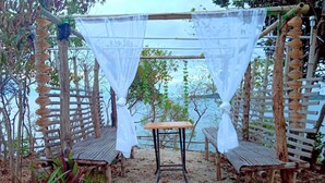 A wooden pergola with white netting, a wooden table, and benches in a coastal setting. - Bolo Beach Santorini (Alaminos)