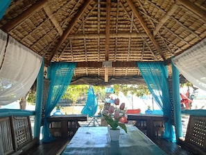 Relax in a tranquil outdoor space with a thatched roof, wooden benches, and lush green surroundings.