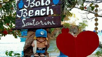 A wooden sign welcoming visitors to Bolo Beach Santorini, featuring a lifeguard figure and a heart-shaped decoration.