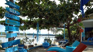 A beachside lounge with a view of the sea, surrounded by potted plants and a signpost with various beach-related words. - Bolo Beach Santorini (Alaminos)