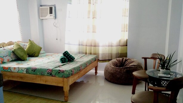 A bedroom with a bed, a chair, a round table, a potted plant, and a window with curtains. - Marie's Sleep Transient House (Alaminos)