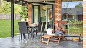 Une terrasse extérieure avec une table et des chaises, un banc en bois et une porte vitrée donnant sur un jardin.
