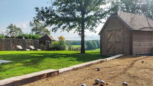 Un cadre extérieur rustique comprenant une grange en bois, un mur de pierre et une zone herbeuse avec un chemin de gravier.