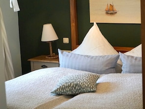 Ein ordentlich bezogenes Bett mit Kissen und einer gestreiften Decke, eine Nachttischlampe und ein gerahmtes Bild eines Segelboots an der Wand.