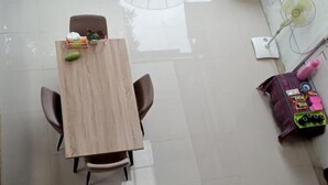 A tiled patio with a wooden table and two chairs, a white chair, and a fan against the wall.