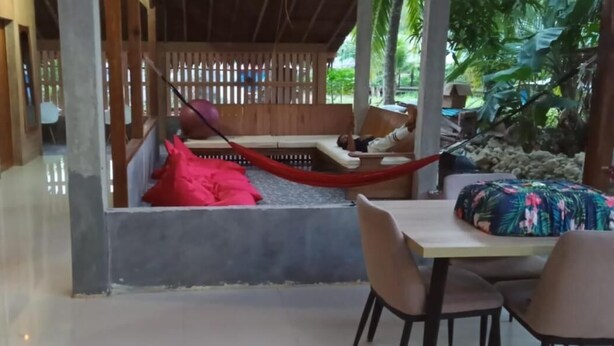 A covered outdoor seating area with a hammock, a wooden bench, and a table with chairs.