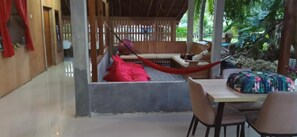Een overdekte buitenruimte met een hangmat, een houten bank en een tafel met stoelen.