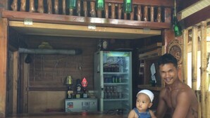 A wooden bar with a sign reading "Mental Health Bagus" and a refrigerator stocked with beverages.