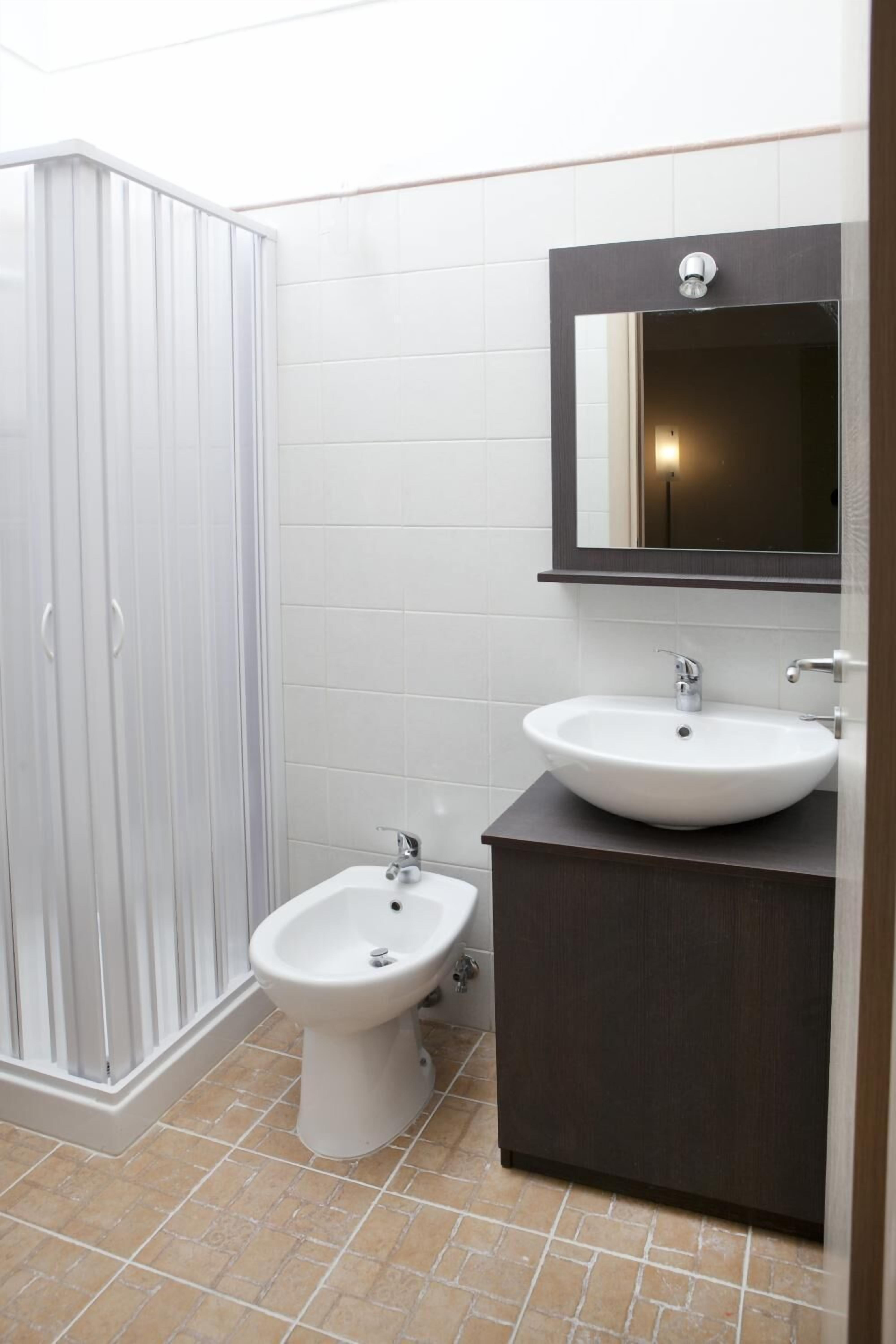 Une salle de bain avec un bidet sur pied blanc, un meuble-lavabo en bois foncé avec un lavabo blanc, et un miroir au-dessus du lavabo.