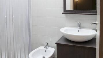 Une salle de bain avec un bidet sur pied blanc, un meuble-lavabo en bois foncé avec un lavabo blanc, et un miroir au-dessus du lavabo.