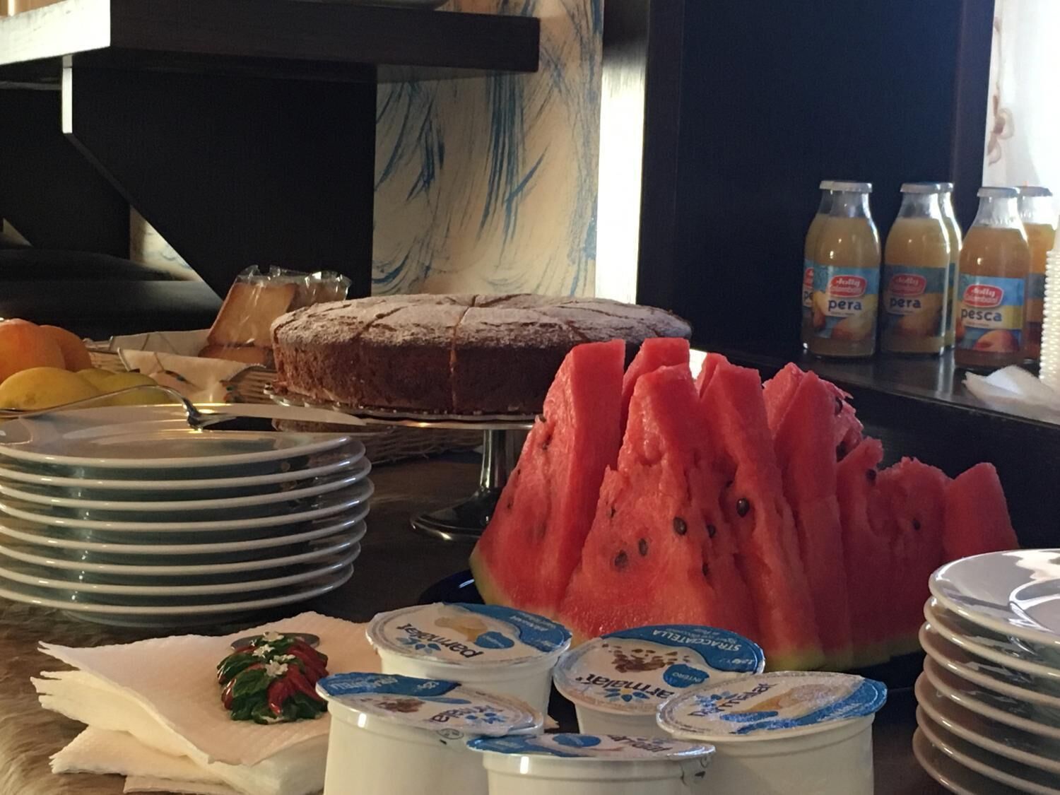 A breakfast buffet with a cake, watermelon, yogurt, and juice.