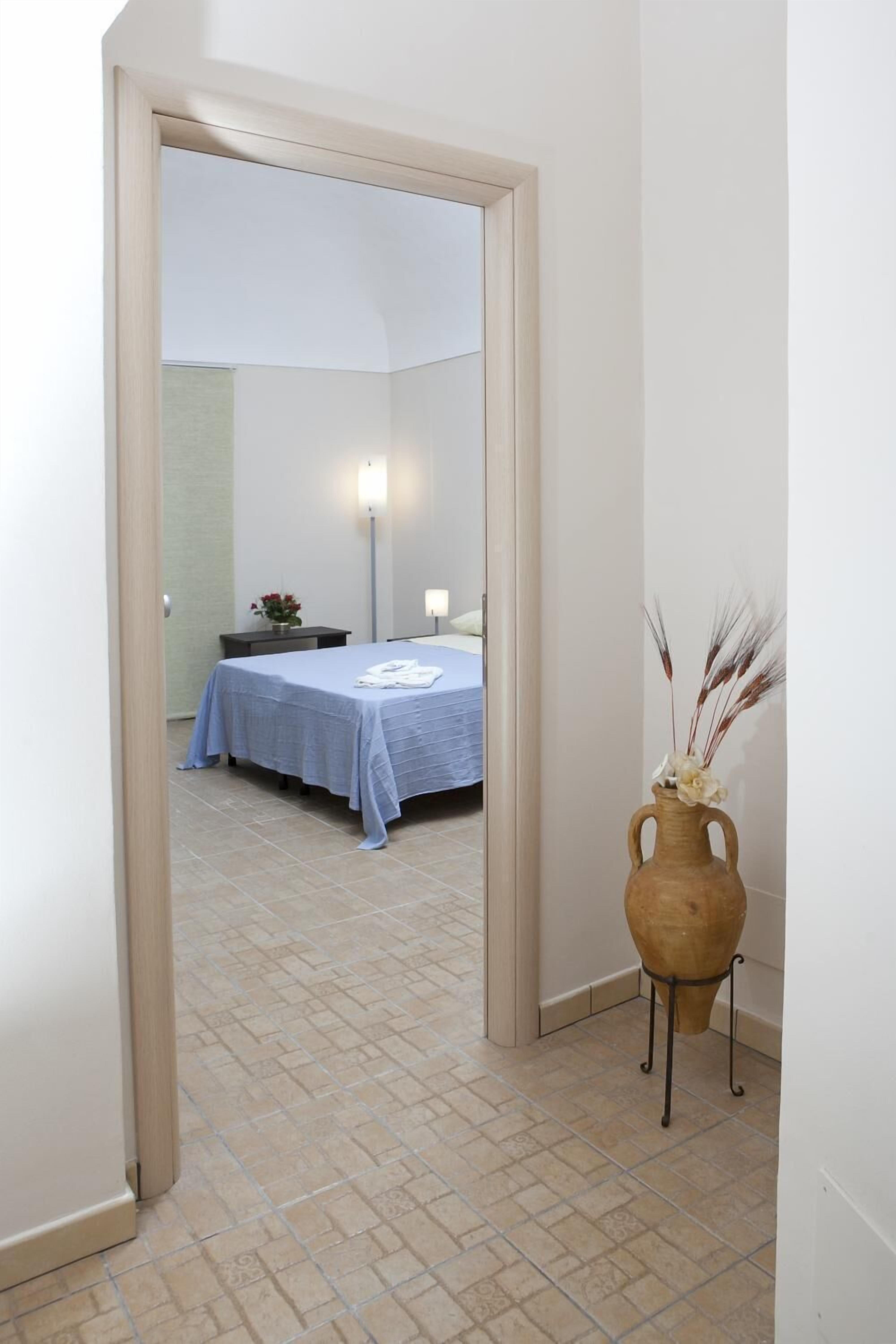 A hotel room with a bed, a nightstand, a vase with flowers, and a mirror.