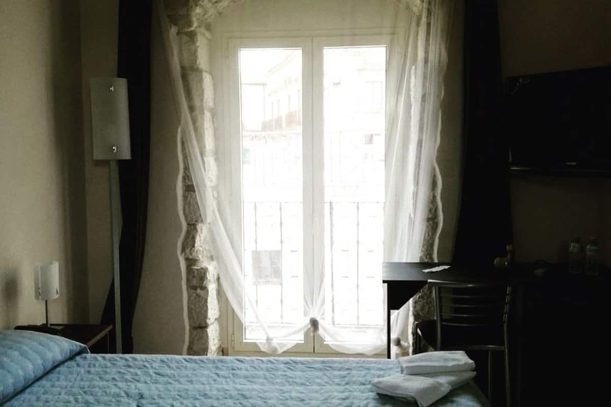 A hotel room with a bed, a desk, a chair, and a window with curtains.