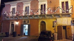 A building with a balcony decorated with string lights, a car parked in front, and a no parking sign. - B&B Dinastia (Monterosso Almo)