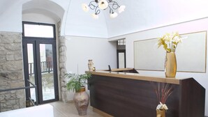 A reception area with a stone wall, a wooden reception desk, and a large mirror. - B&B Dinastia (Monterosso Almo)