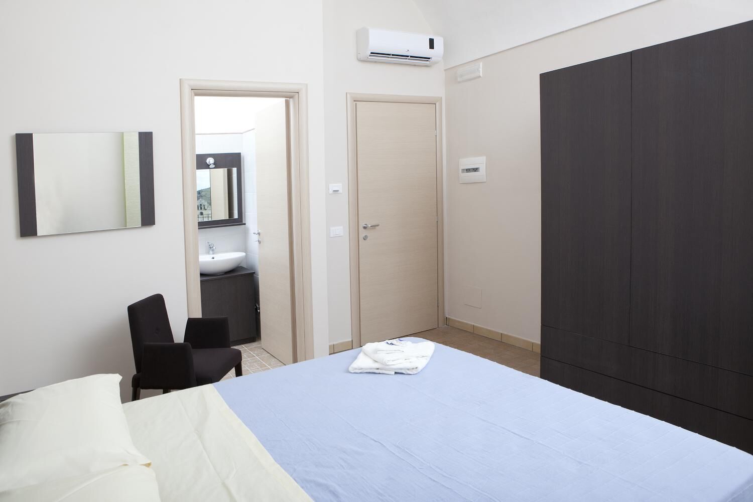 A bedroom with a bed, a desk, a chair, a wardrobe, and a bathroom visible through an open door.