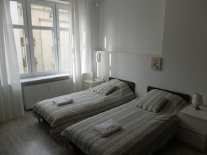 Une chambre avec deux lits, une fenêtre avec des rideaux, une table de chevet avec une lampe et un radiateur.