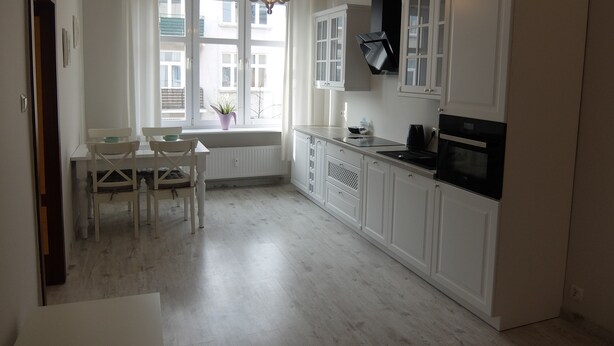 Une cuisine moderne avec des meubles blancs, un coin repas comprenant une table et des chaises, et une fenêtre donnant sur les bâtiments voisins.