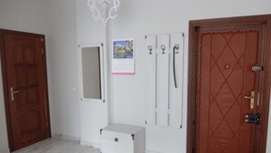Une pièce avec une porte en bois, une armoire blanche, un porte-manteau blanc, un calendrier et une porte dotée d’une serrure.