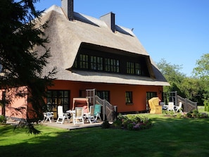 A thatched-roof house with a wooden staircase leading to a porch.