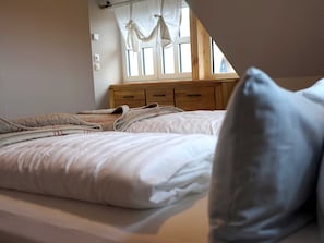A bedroom with two beds, a wooden dresser, and a window with curtains.