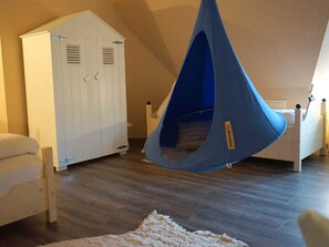 Una stanza con una poltrona sacco blu appesa, un armadio bianco e un letto con testiera in legno.