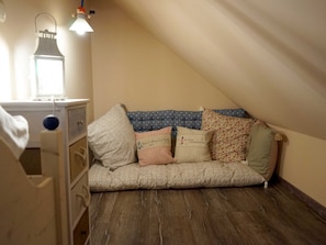 A cozy attic bedroom with a sloped ceiling, a wooden floor, and a sofa with nautical-themed pillows.