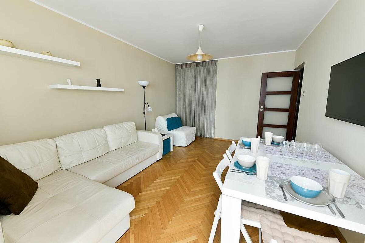 Un salon moderne avec un canapé blanc, une table à manger dressée pour quatre personnes et un ventilateur de plafond.