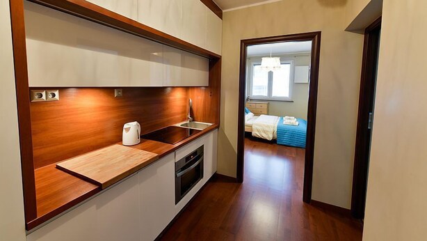 Eine kompakte Küche mit Holzarbeitsplatten, einem eingebauten Backofen und einem Spülbecken. Ein Flur führt zu einem Schlafzimmer mit einem Bett und einem Fenster.