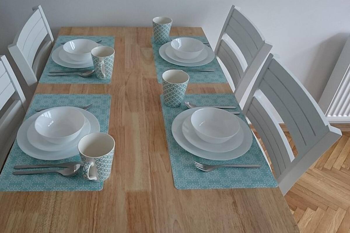 Une table à manger dressée avec de l’assiette, des bols et des couverts blancs, le tout posé sur des sets de table à motifs.