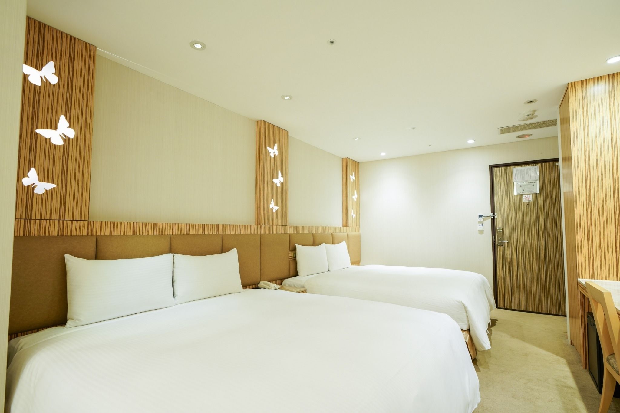 Une chambre d’hôtel avec deux lits, une tête de lit en bois, une porte en bois et un mur décoré de motifs de papillons.