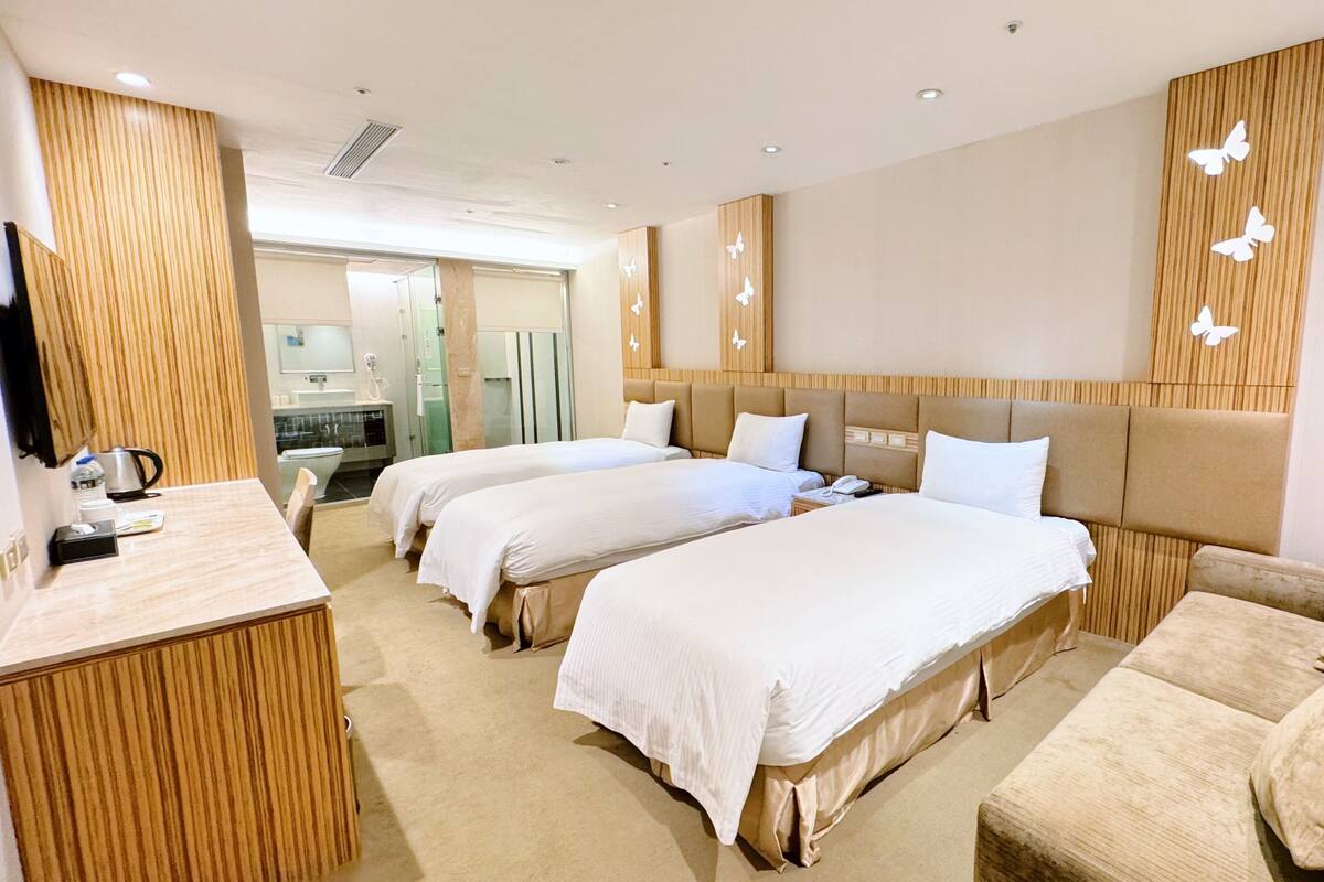 A hotel room with two beds, a sofa, a desk, and a bathroom visible through an open door.