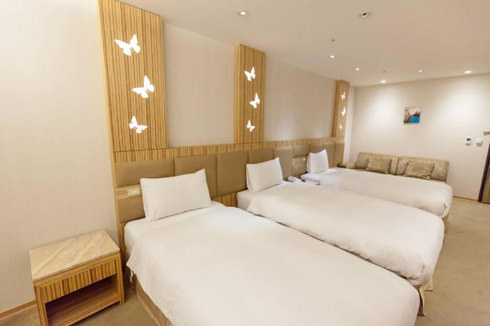 Habitación de hotel con tres camas, cabecera de madera y lámparas con forma de mariposa.