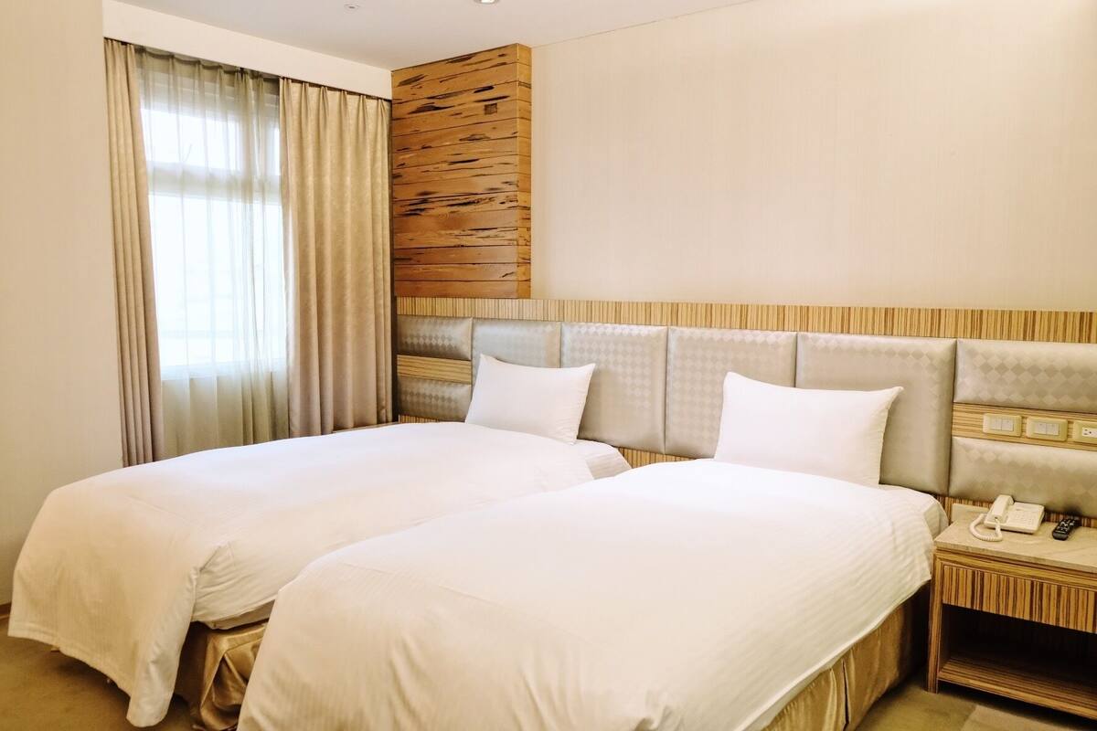 A hotel room with two beds, a wooden accent wall, and a nightstand with a phone and remote.