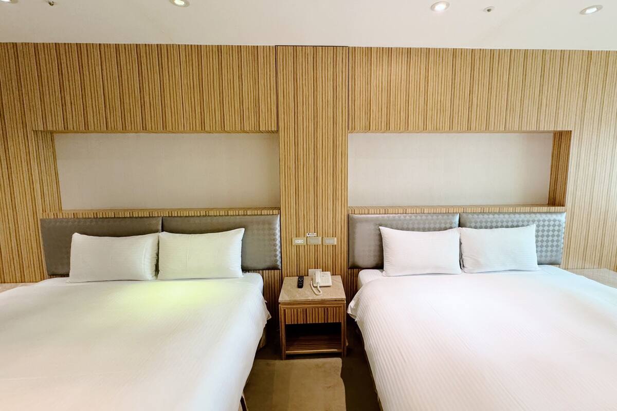 A hotel room with two beds, a nightstand with a phone, and a wall with vertical wooden panels.