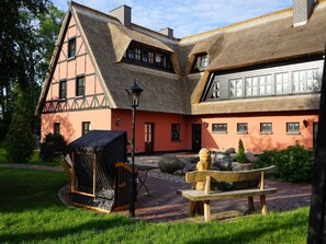 Un bâtiment traditionnel avec un toit de chaume, un banc en bois et un petit jardin.