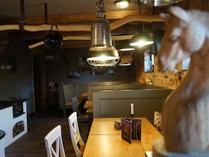 L’intérieur d’un restaurant avec des poutres en bois, des luminaires suspendus, une cheminée et un présentoir à menus.