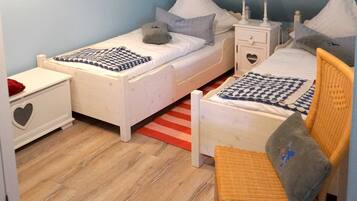 Ein Kinderzimmer mit zwei Einzelbetten, einem kleinen Stuhl, einem Nachttisch mit herzförmiger Schublade und einer Lampe mit Anker-Design.
