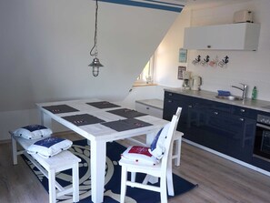 Une cuisine compacte avec des meubles blancs, une table à manger avec quatre chaises et un petit îlot central doté d’un évier et d’une machine à café.
