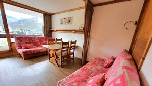 A cozy room with a wooden floor, a dining table with chairs, a sofa, and a window with a view of mountains. - Ski-in studio in the heart of Les Menuires, pets allowed (Les Menuires)