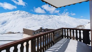 Montaña nevada con barandal de madera y un edificio al fondo.